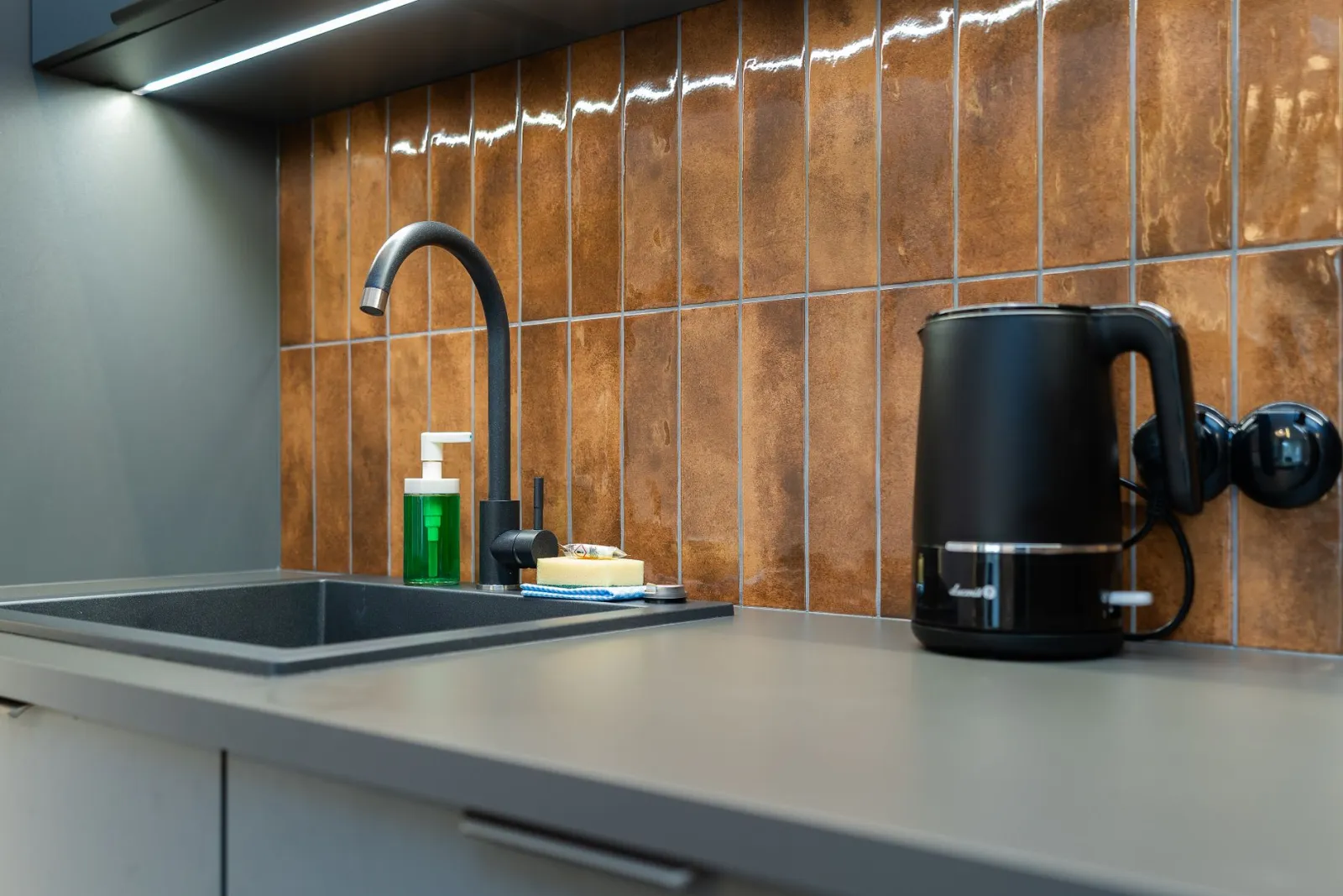 Contemporary kitchen counter setup with a sink, soap dispenser, and electric kettle.